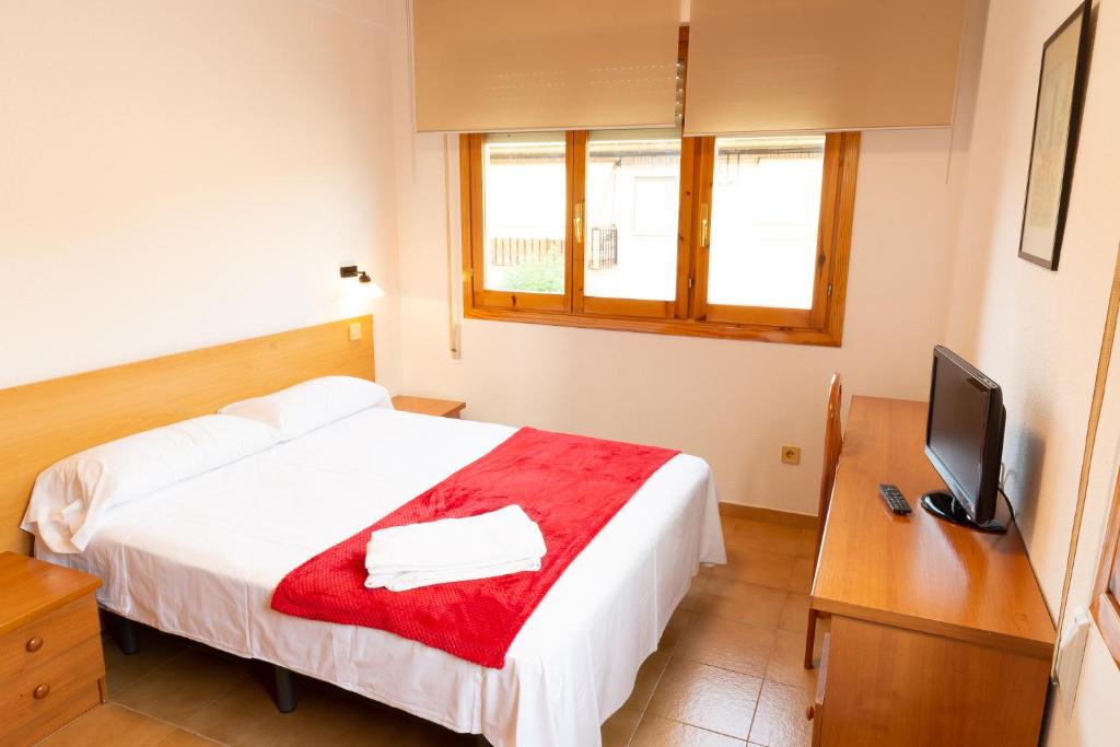 a bedroom with a bed with a red blanket and a television at Hostal Legaz in Funes