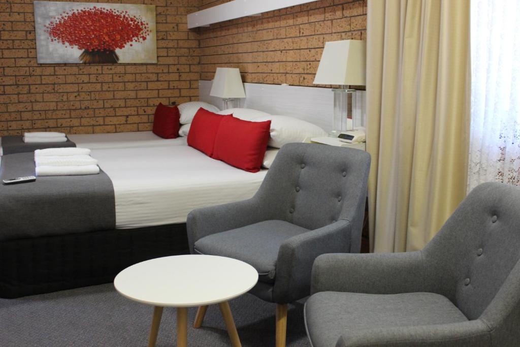 a hotel room with a bed and two chairs and a table at Golden Harvest Motor Inn Moree in Moree