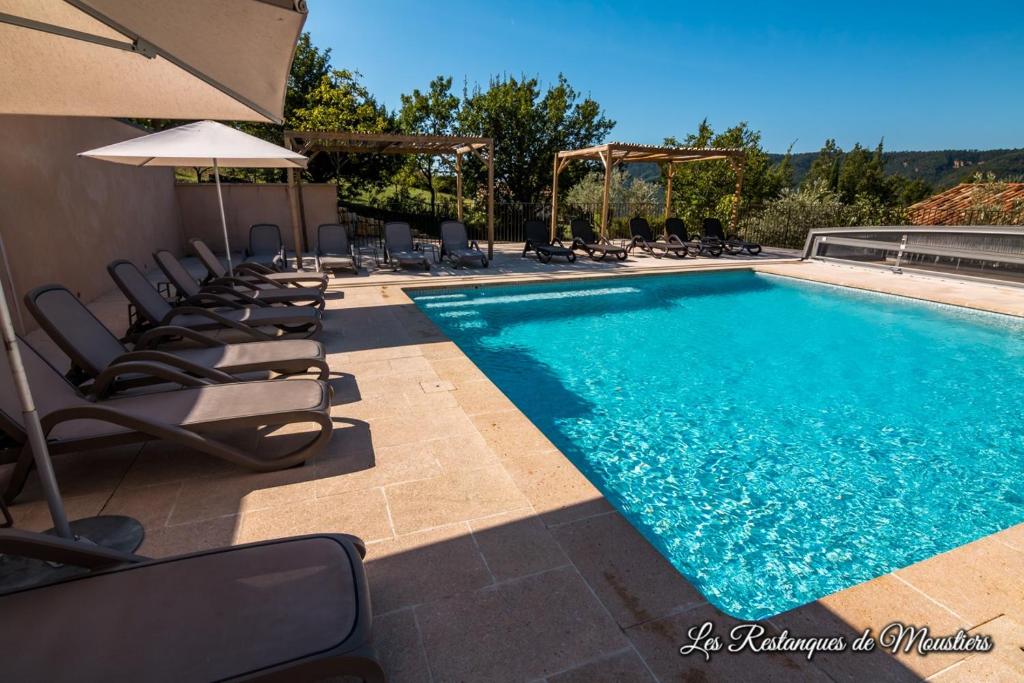 a swimming pool with lounge chairs and an umbrella at Hotel Les Restanques De Moustiers in Moustiers-Sainte-Marie