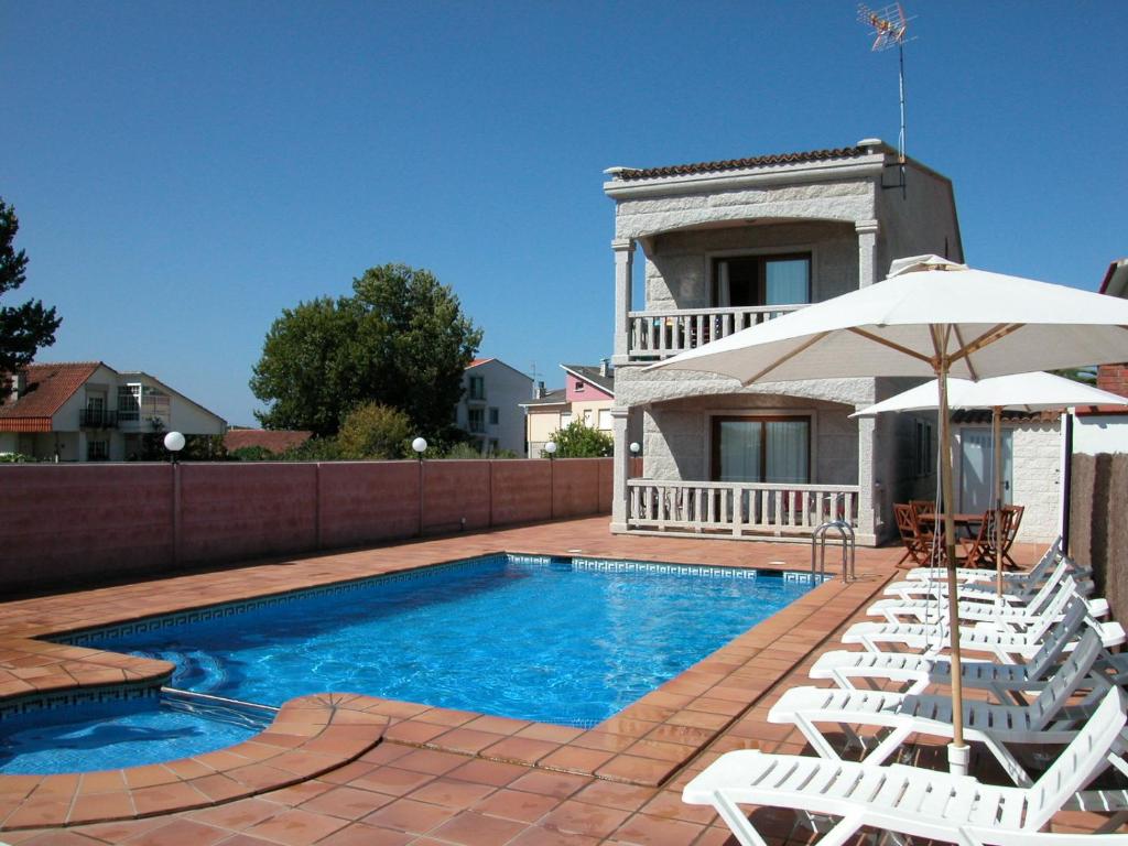 ein Pool mit Stühlen und einem Sonnenschirm und ein Haus in der Unterkunft Apartamentos Coral Do Mar III in Montalvo
