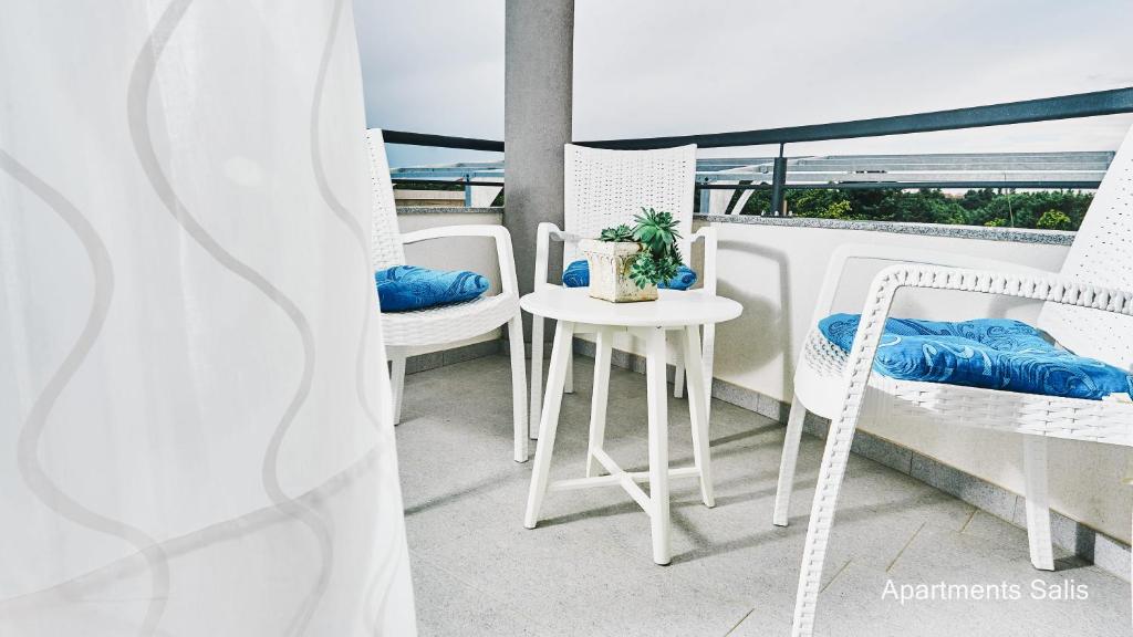a balcony with white chairs and a table and a window at Salis Apartments in Vrsi