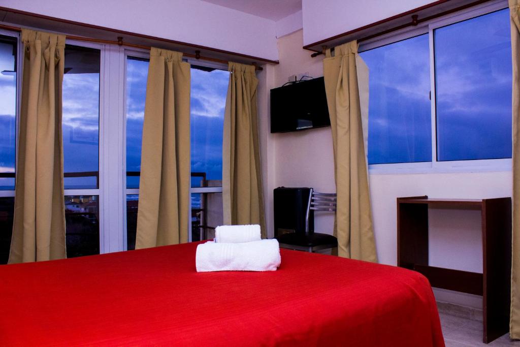 1 dormitorio con cama roja y ventanas grandes en Hotel San Remo Majestic, en Mar de Ajó