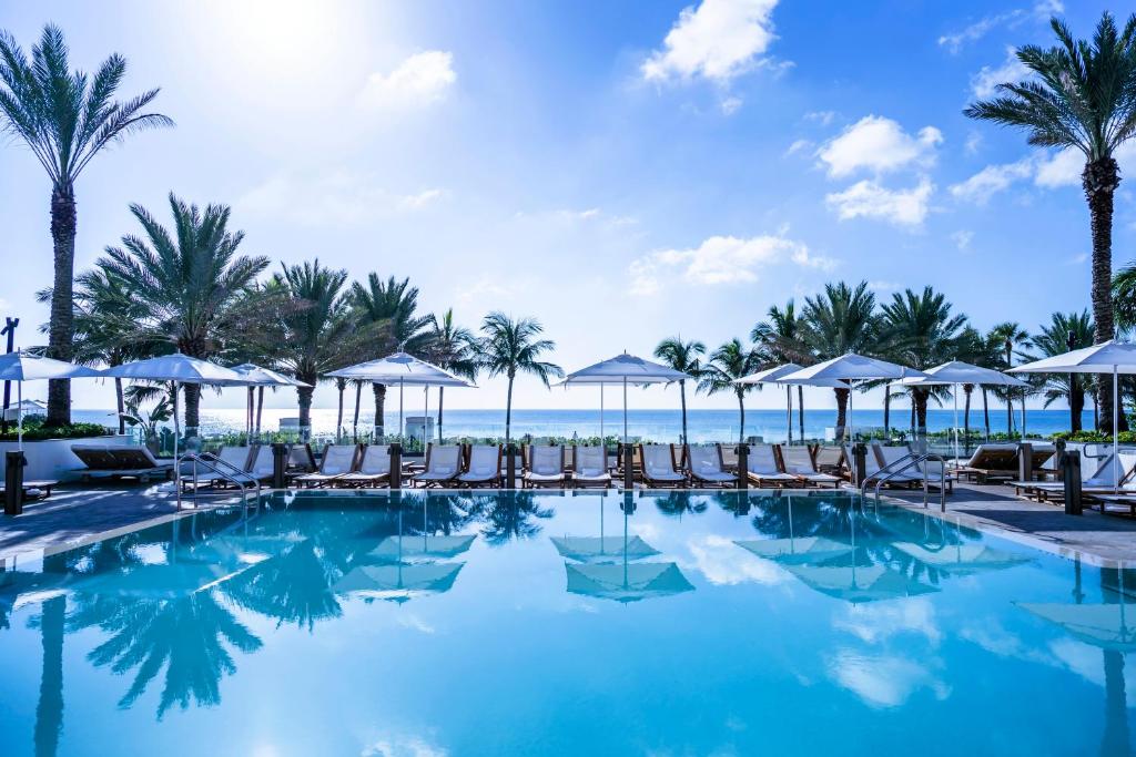 una piscina en la playa con sillas y sombrillas en Nobu Hotel Miami Beach, en Miami Beach