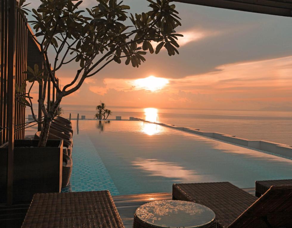 An infinity pool stretches toward the ocean at sunset, with shaded seating and a small table in the foreground.