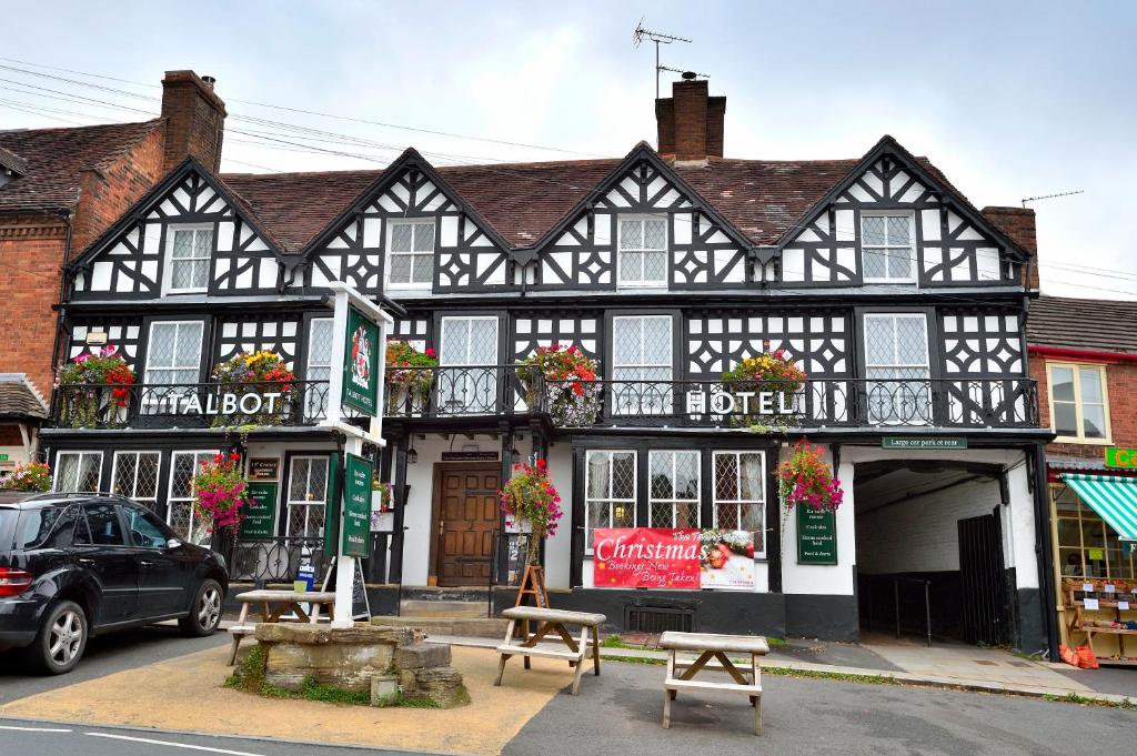 The Talbot Hotel في Cleobury Mortimer: مبنى أسود وبيضاء مع مقاعد أمامه