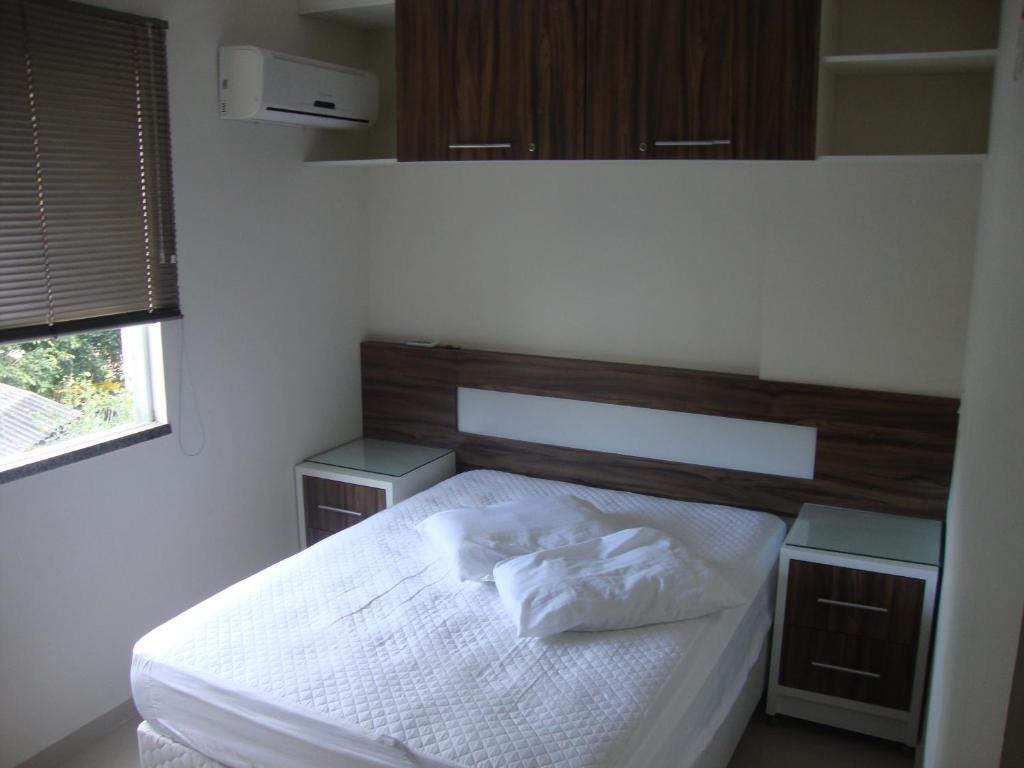 Un dormitorio con una cama con sábanas blancas y una ventana. en apartamento aluguel temporada bombinhas, en Bombinhas