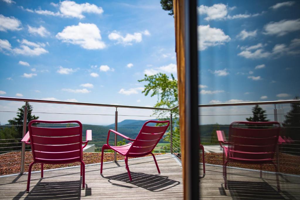 three red chairs sitting on a deck with a view at Le Holzberg et ses Suites in Osenbach