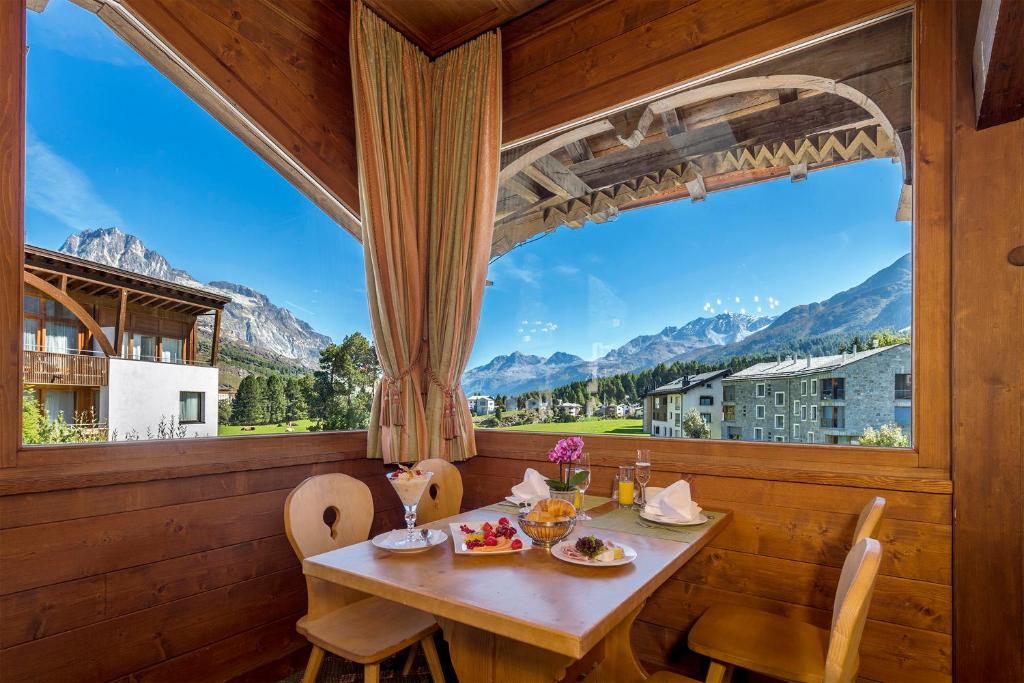 een eetkamer met een tafel en een groot raam bij Schweizerhaus Swiss Quality Hotel in Maloja