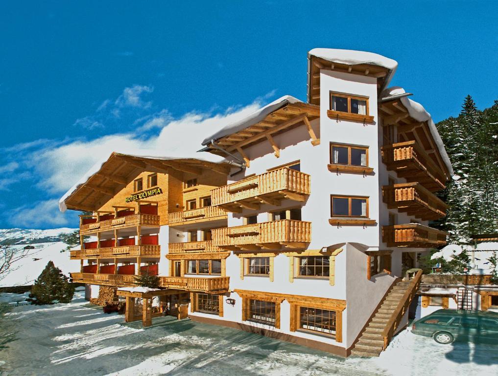 duży budynek z drewnianymi balkonami w śniegu w obiekcie Hotel Olympia w mieście Pettneu am Arlberg