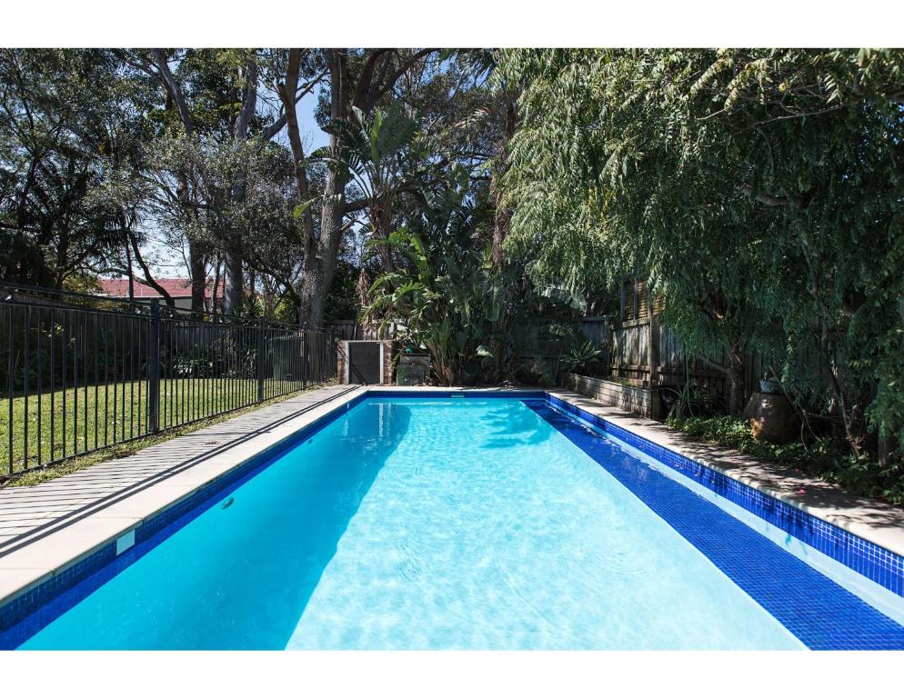 a blue swimming pool with trees and a fence at Comfy family home in chill beachside neighbourhood in Sydney