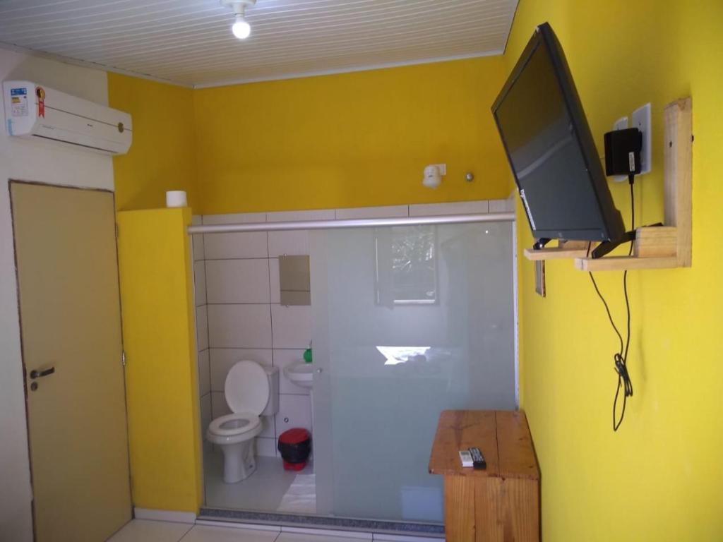 a bathroom with a toilet and a tv on a wall at Pousada Aritibe in Ilha de Boipeba
