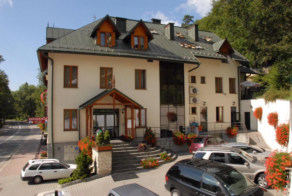 una gran casa blanca con coches aparcados en un aparcamiento en Hotel Saol en Krynica Zdrój