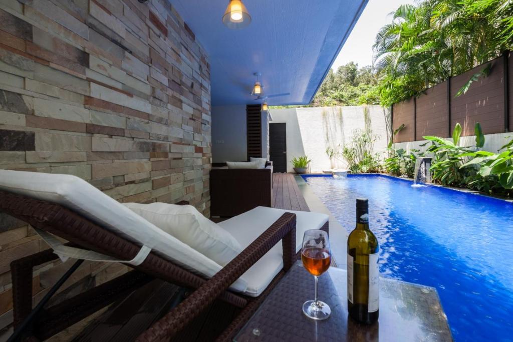 uma garrafa de vinho sentada numa mesa ao lado de uma piscina em Frangipani Villa em Anjuna