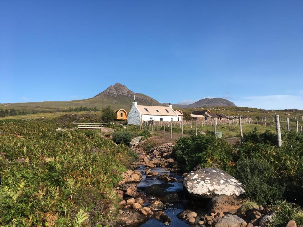 a house on a hill next to a stream at Acheninver Hostel in Achiltibuie