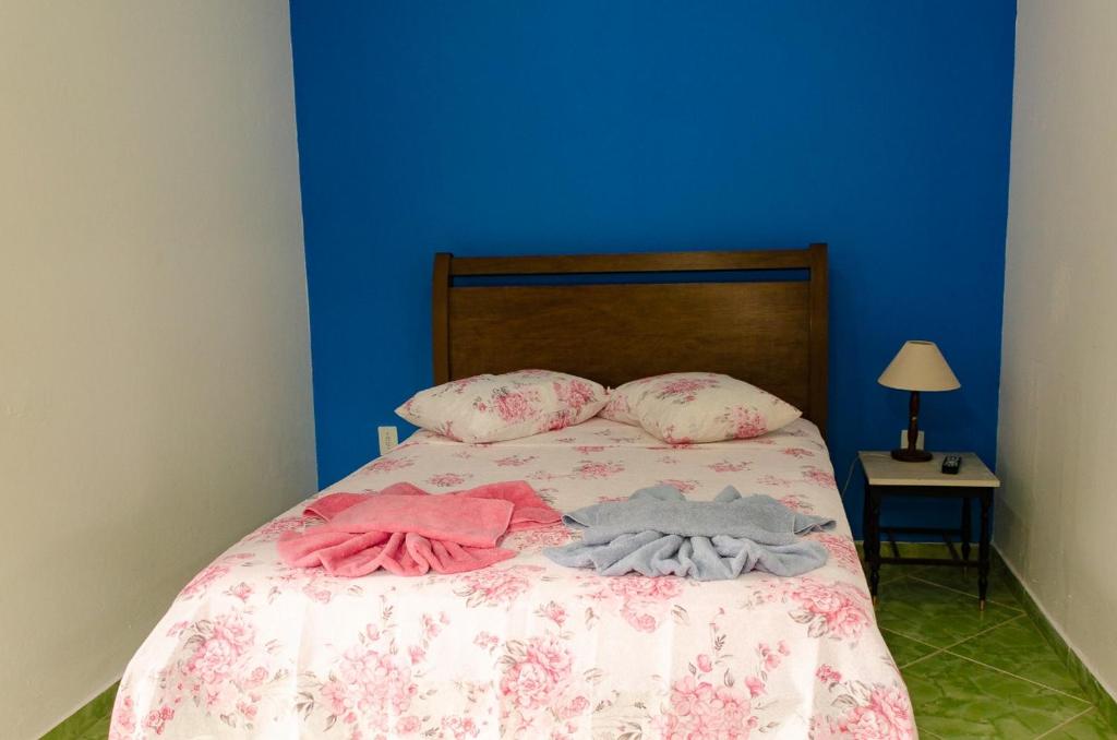 a bed with clothes on it with a blue wall at Chalé saí azul in Penedo