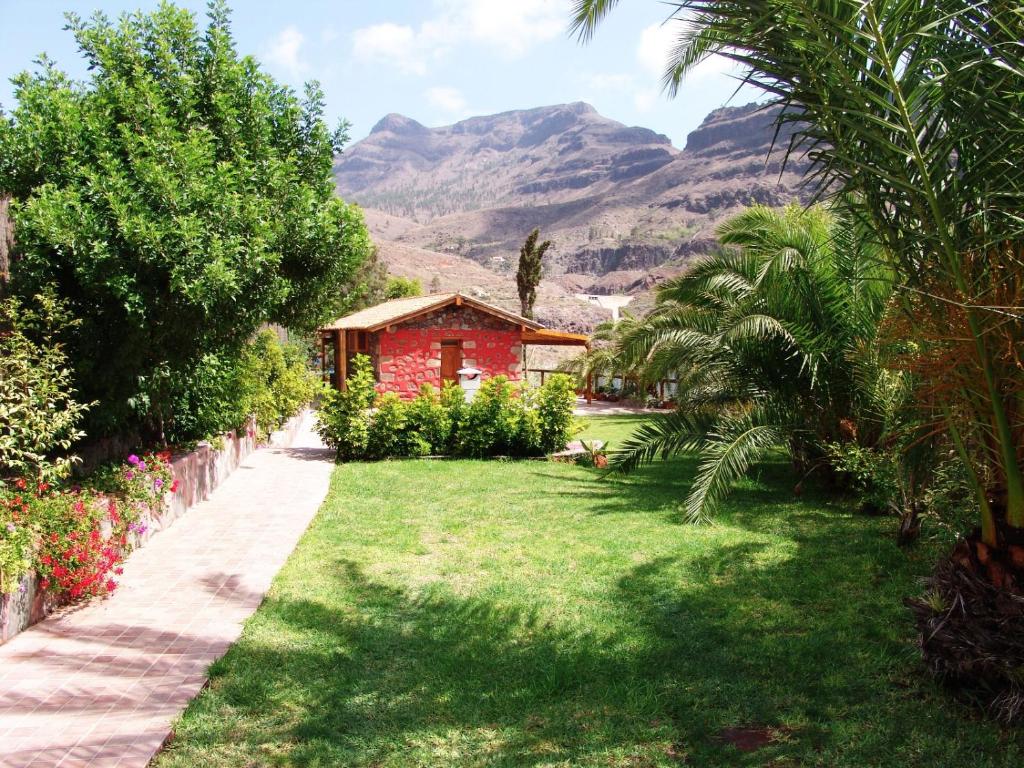 a garden with a red house and mountains in the background at Casa Romantica in Los Palmitos
