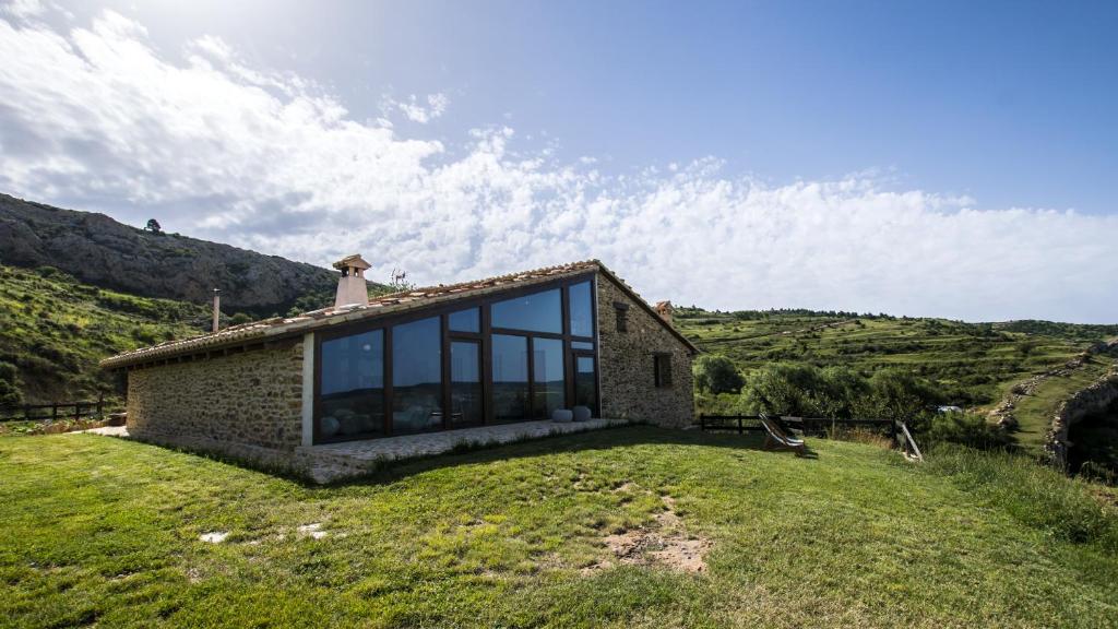 una casa de piedra en una colina con ventanas de cristal en Masía el Cabrero en Villarroya de los Pinares