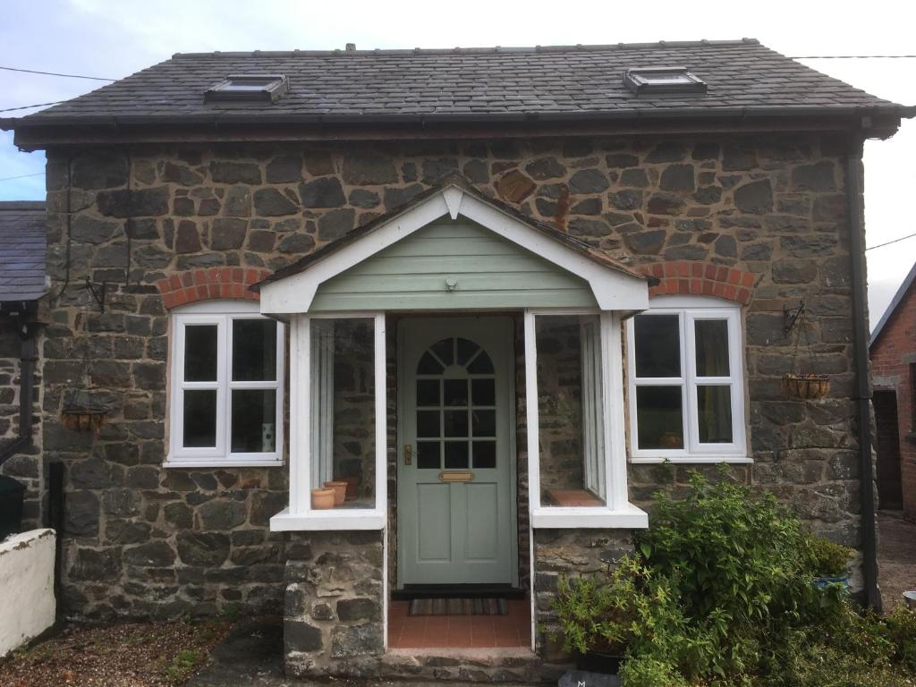 ウェルシュプールにあるMaesnewydd Cottageの緑のドアと窓が備わる石造りのコテージ