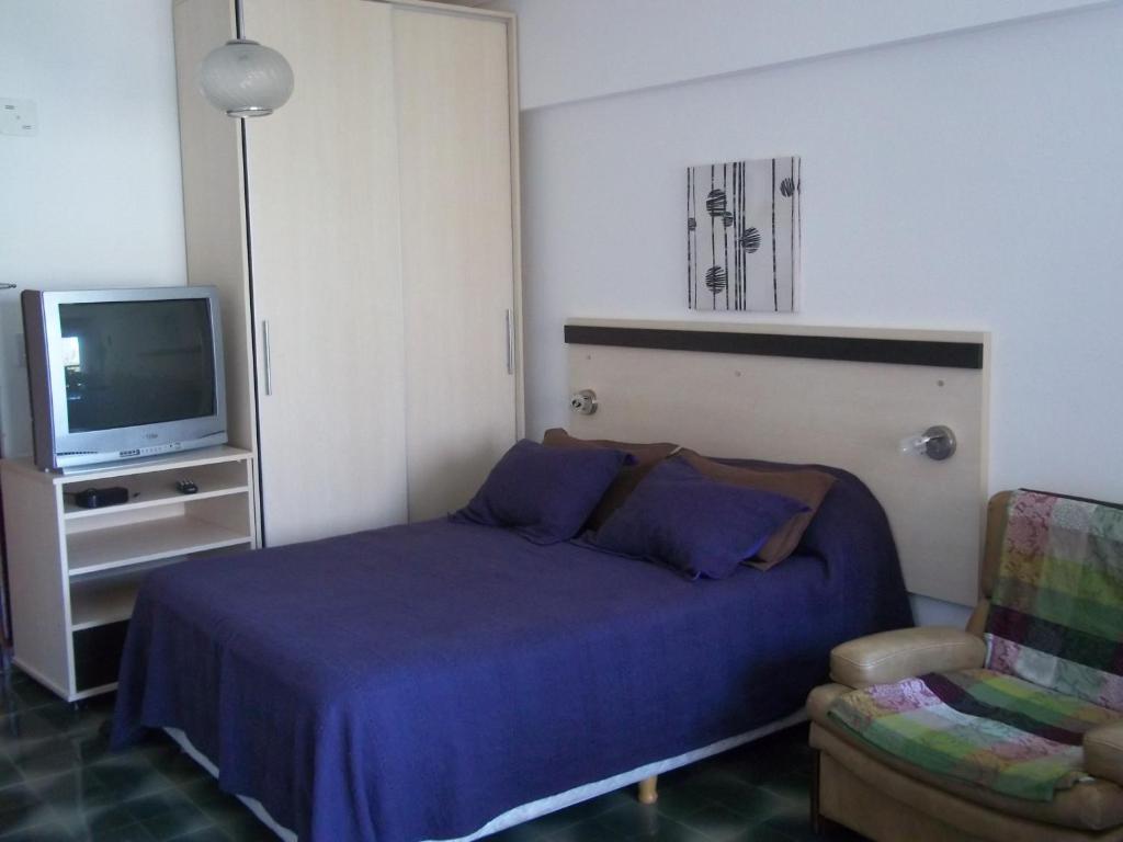 1 dormitorio con 1 cama, TV y silla en Departamento La Perla en Mar del Plata