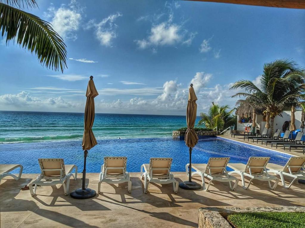 uma piscina com cadeiras e guarda-sóis junto ao oceano em Cozy and Modern em Cancún