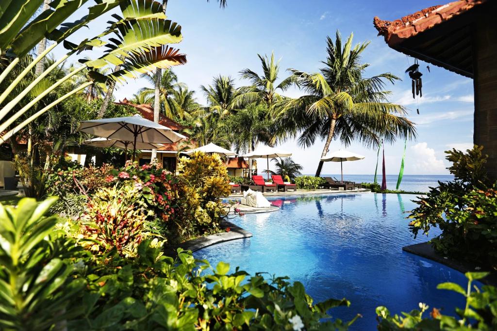 una piscina in un resort con palme e oceano di Teluk Karang Dive & Spa Resort a Tejakula