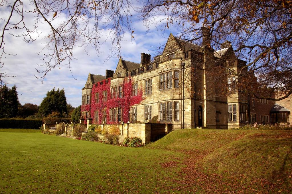 una casa vieja con un árbol rojo delante de ella en Gisborough Hall Hotel, en Guisborough