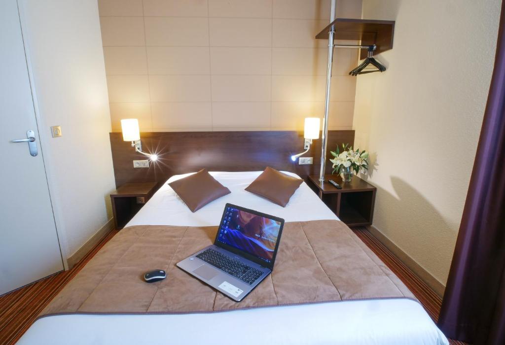 laptopa siedzącego na łóżku w obiekcie Hotel Inn Design Poitiers Sud w mieście Poitiers