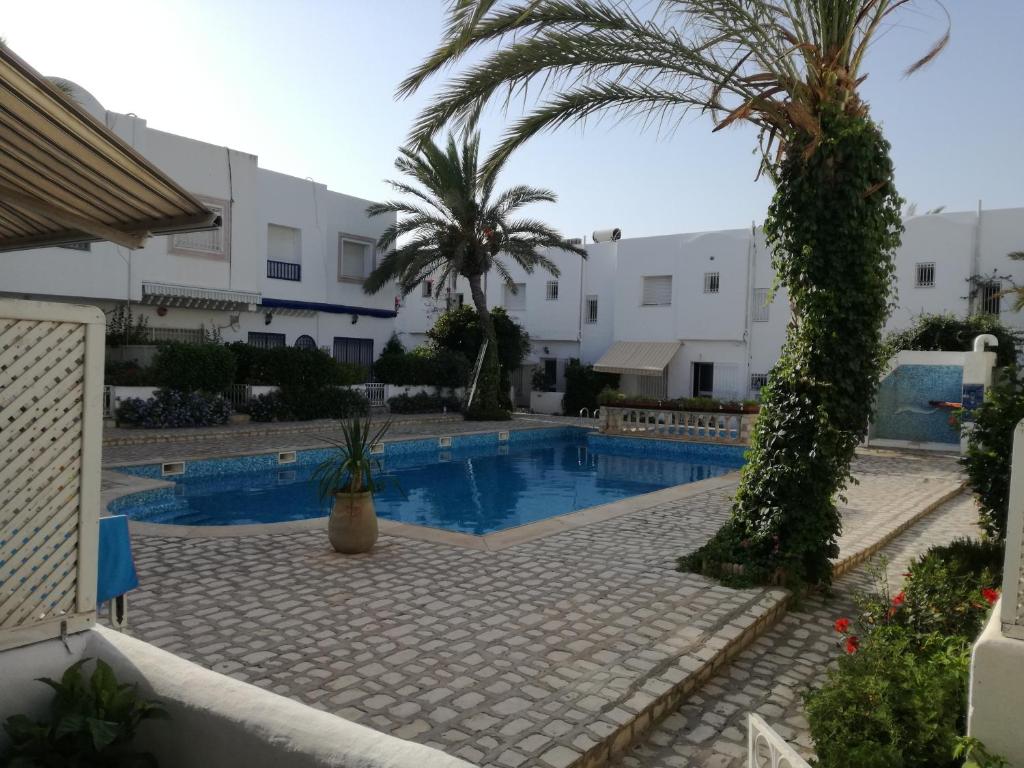 a swimming pool with a palm tree and buildings at Sonny Apartment in Hammamet