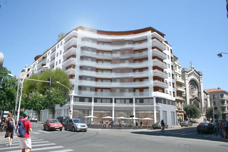 un grand bâtiment blanc dans une rue de la ville avec des voitures dans l'établissement Promenade Gambetta, à Nice