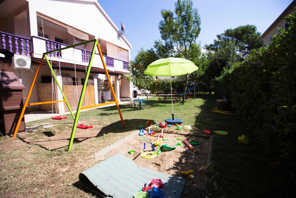 un parque infantil con sombrilla y juguetes en el patio en Apartments Lorena en Privlaka