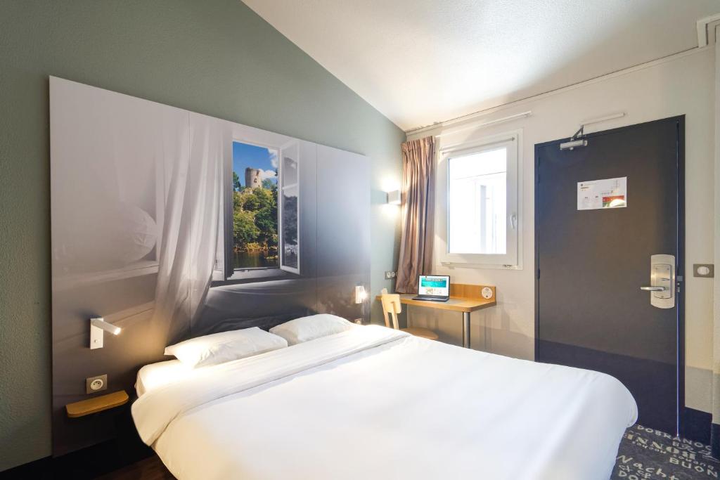 a bedroom with a large white bed and a window at B&B HOTEL CHATEAUROUX Aéroport in Déols