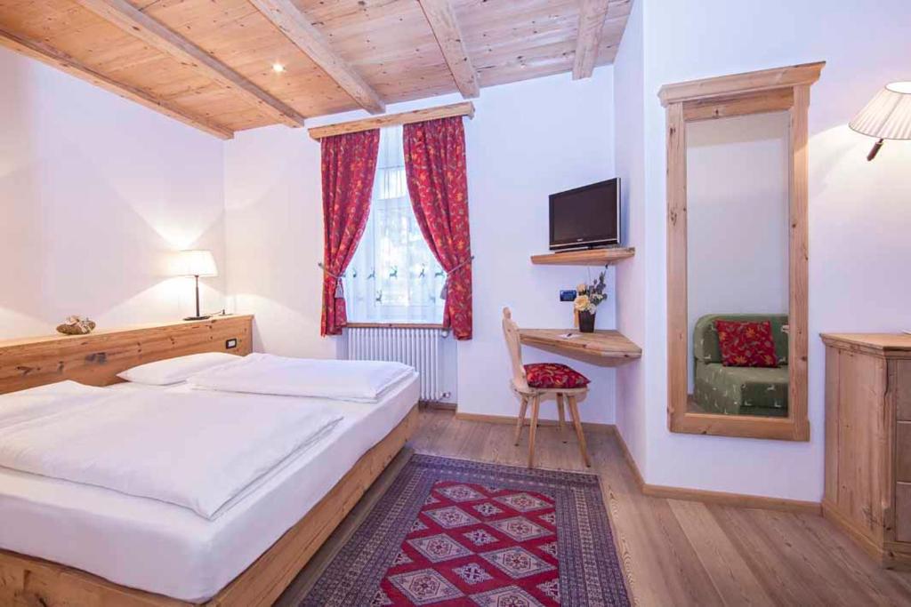 a bedroom with a bed and a window and a chair at Hotel Corona Krone in Selva di Val Gardena