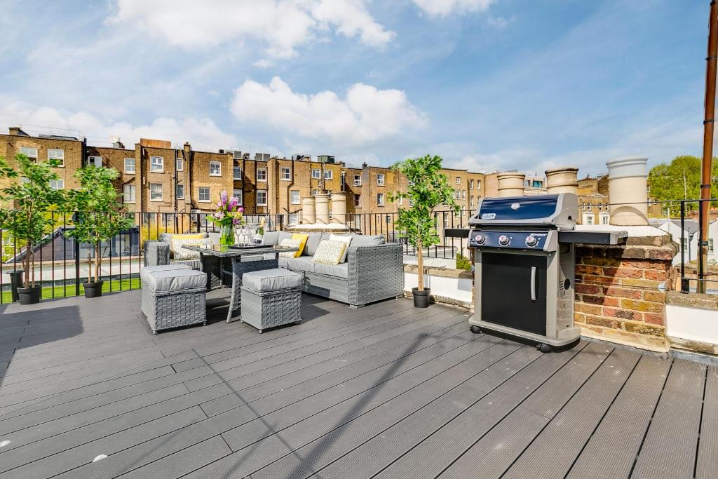 a patio with a grill and furniture on a deck at Superb 3 Bed/Bath Luxury + Ibiza Roof Terrace in London