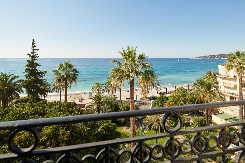 - une vue sur la plage bordée de palmiers et l'océan dans l'établissement Hôtel Vacances Bleues Royal Westminster, à Menton