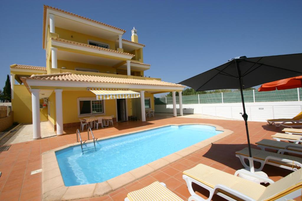 a villa with a swimming pool with chairs and an umbrella at Villa vista mar e piscina in Fuzeta