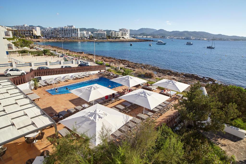 una piscina con sombrillas blancas y una playa en Sol Bahía Ibiza Suites, en San Antonio