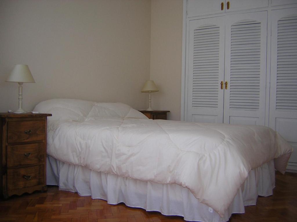 a bedroom with a white bed with a nightstand and two white doors at Corrientes y Esmeralda in Buenos Aires