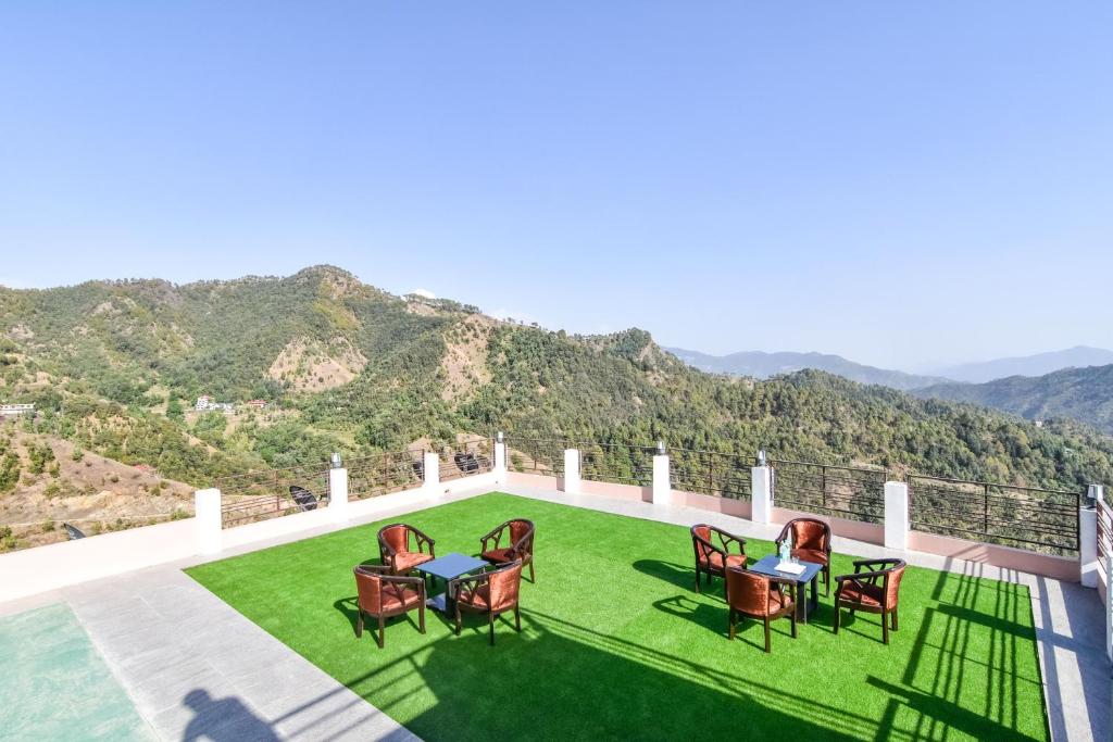 eine Terrasse mit Stühlen und Tischen auf einer grünen Wiese in der Unterkunft Hotel Kaithli Hills Shimla in Shimla