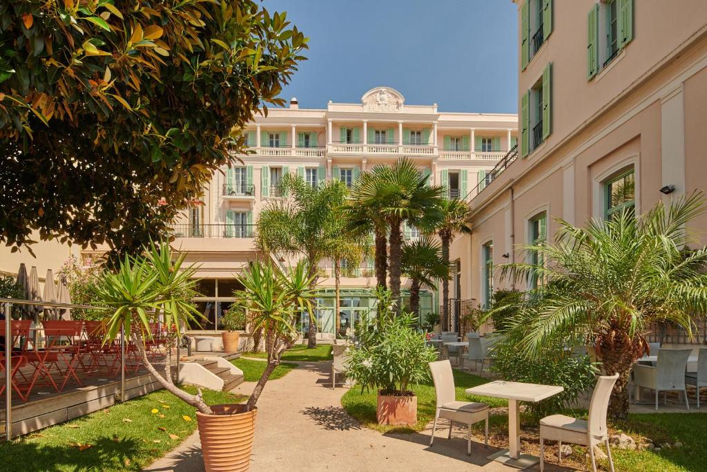 un bâtiment avec des palmiers, une table et des chaises dans l'établissement Hôtel Vacances Bleues Balmoral, à Menton