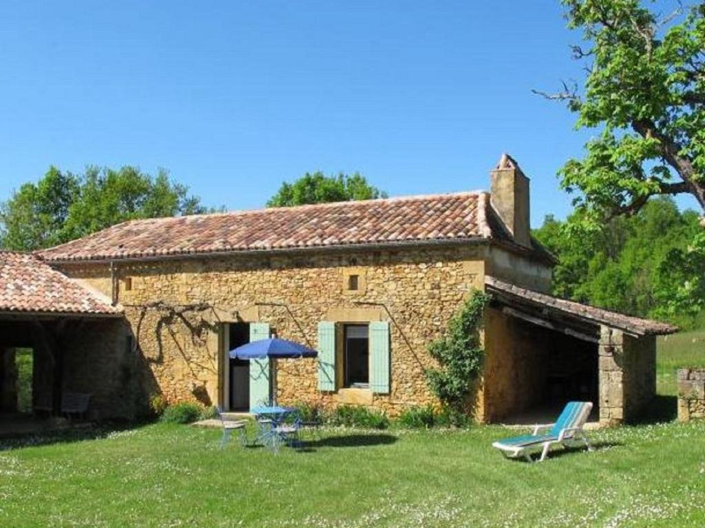 a stone house with a table and a blue umbrella at Comfortable holiday home with garden in Sainte-Croix-de-Beaumont