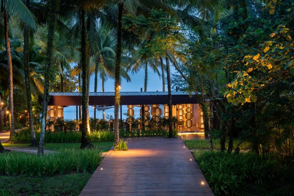 a wooden walkway leading to a building with palm trees at The Sarojin in Khao Lak