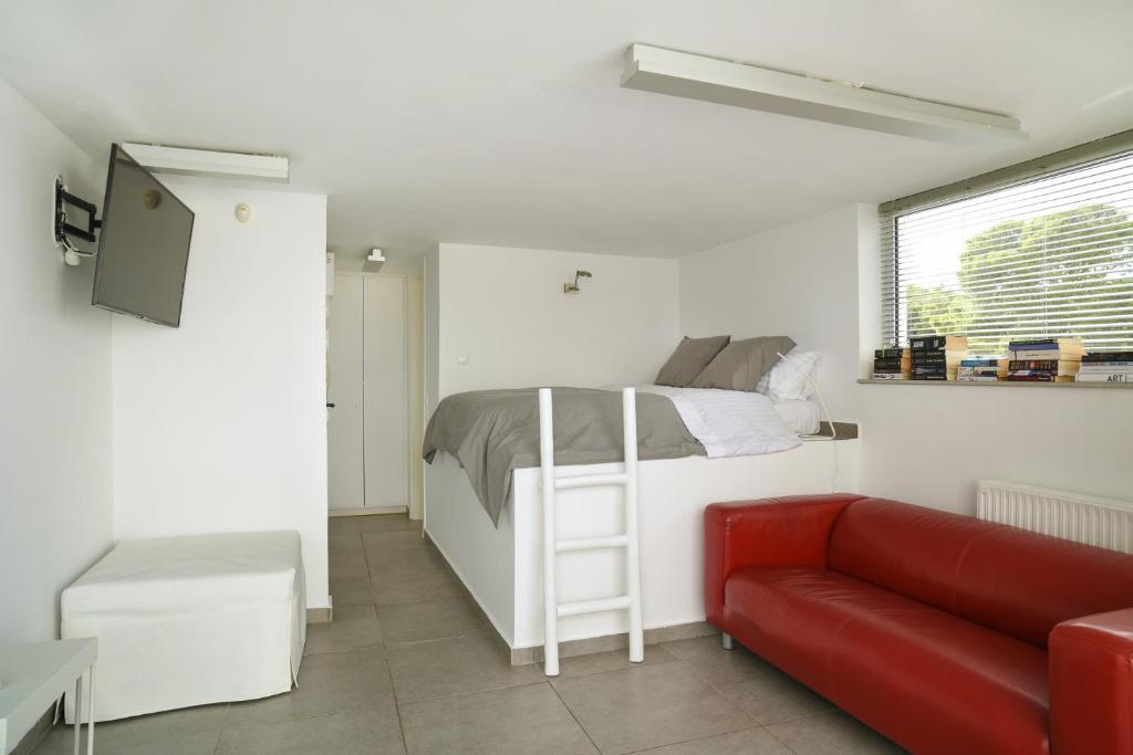 a white bedroom with a bed and a red couch at the coolest loft and terrace-varkiza sea view in Varkiza