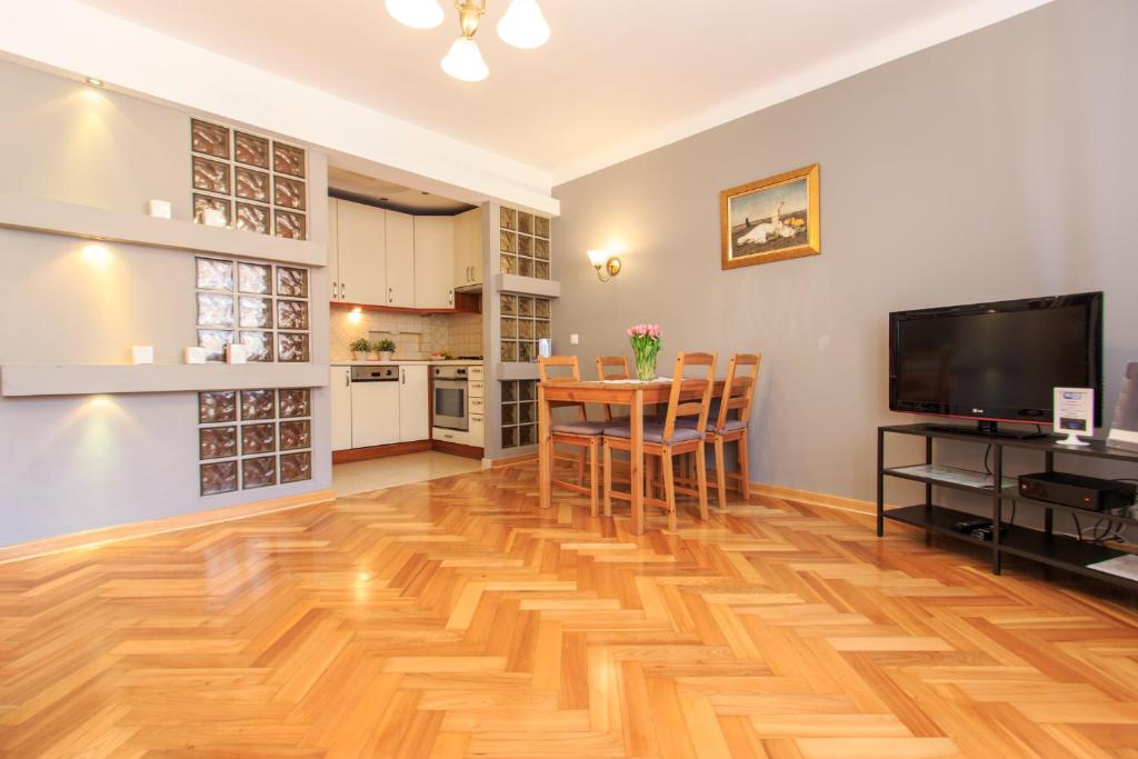 a living room with a wooden floor and a table and a television at Rental Apartments Szeroki Dunaj in Warsaw