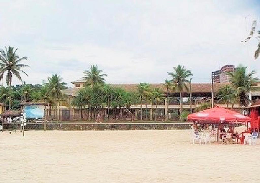 uma praia com mesas e guarda-sóis e palmeiras em Residências Garcez, paraíso à beira da praia Enseada, Guarujá no Guarujá