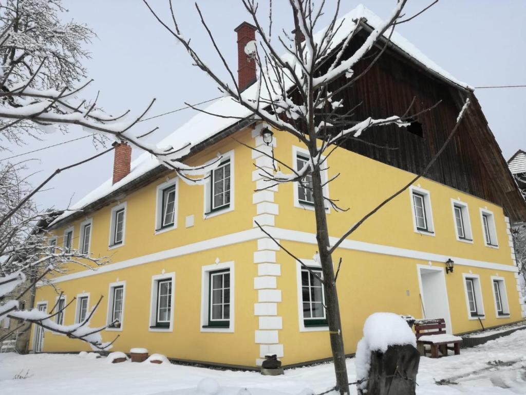 a yellow house with a wooden roof in the snow at Wastlhof am Kreischberg in Lutzmannsdorf
