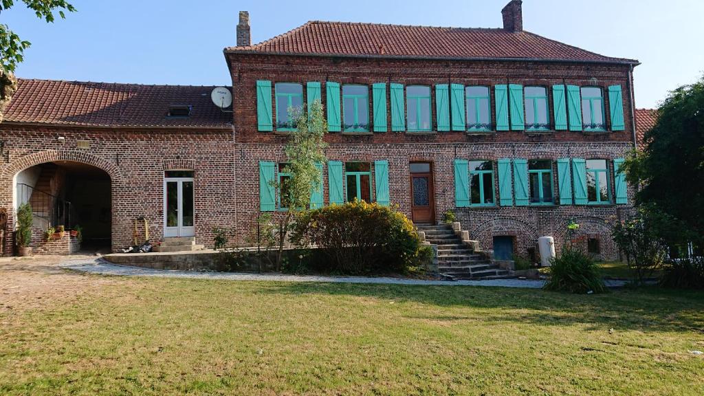 duży ceglany dom z niebiesko-zielonymi oknami w obiekcie Les Chambres du Relais w mieście Liettres