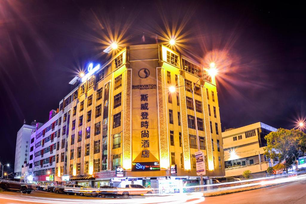 un gran edificio amarillo con una torre de reloj por la noche en Shervinton Executive Boutique Hotel, en Tawau