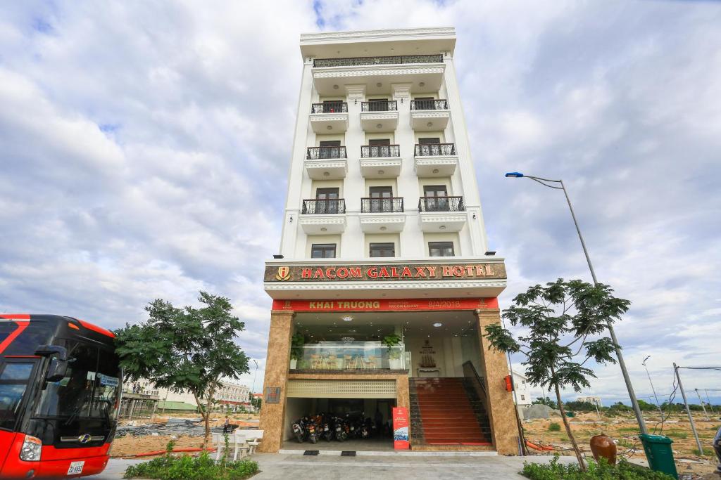 un autobús rojo estacionado frente a un edificio blanco en Hacom Galaxy Hotel, en Phan Rang