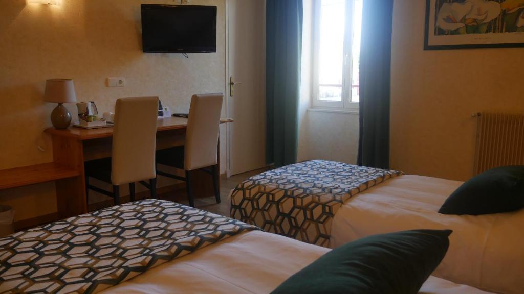 a hotel room with two beds and a desk with a television at Logis Le Saint Cyr in Montmelard