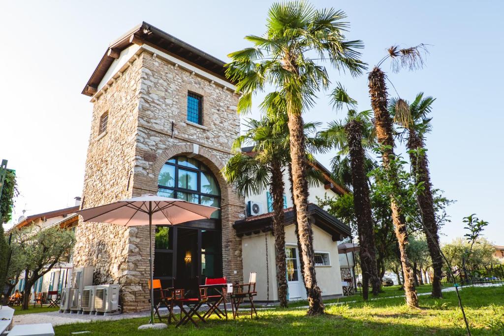 un bâtiment avec des palmiers et une table avec un parasol dans l'établissement Villa Colli Storici, à Desenzano del Garda